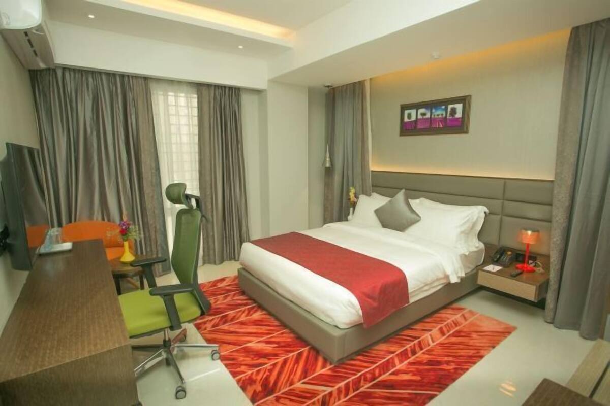 Habitación de hotel con cama, escritorio, silla, mesita de noche y televisión instalada en la pared.