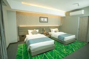 Habitación de hotel con dos camas, alfombra verde estampada, diseño de pared en patrón de espiga y un cuadro enmarcado sobre las camas.