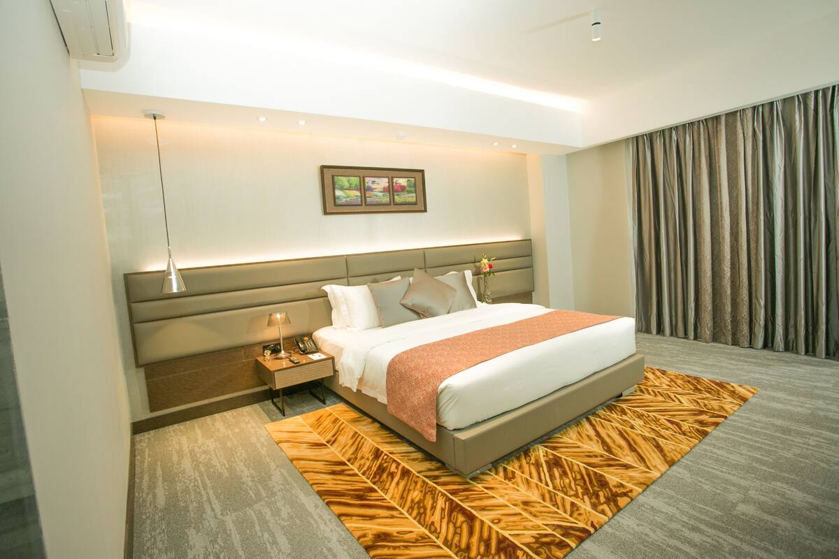 A modern hotel room with a large bed, a nightstand, a wall-mounted picture, and a patterned rug.