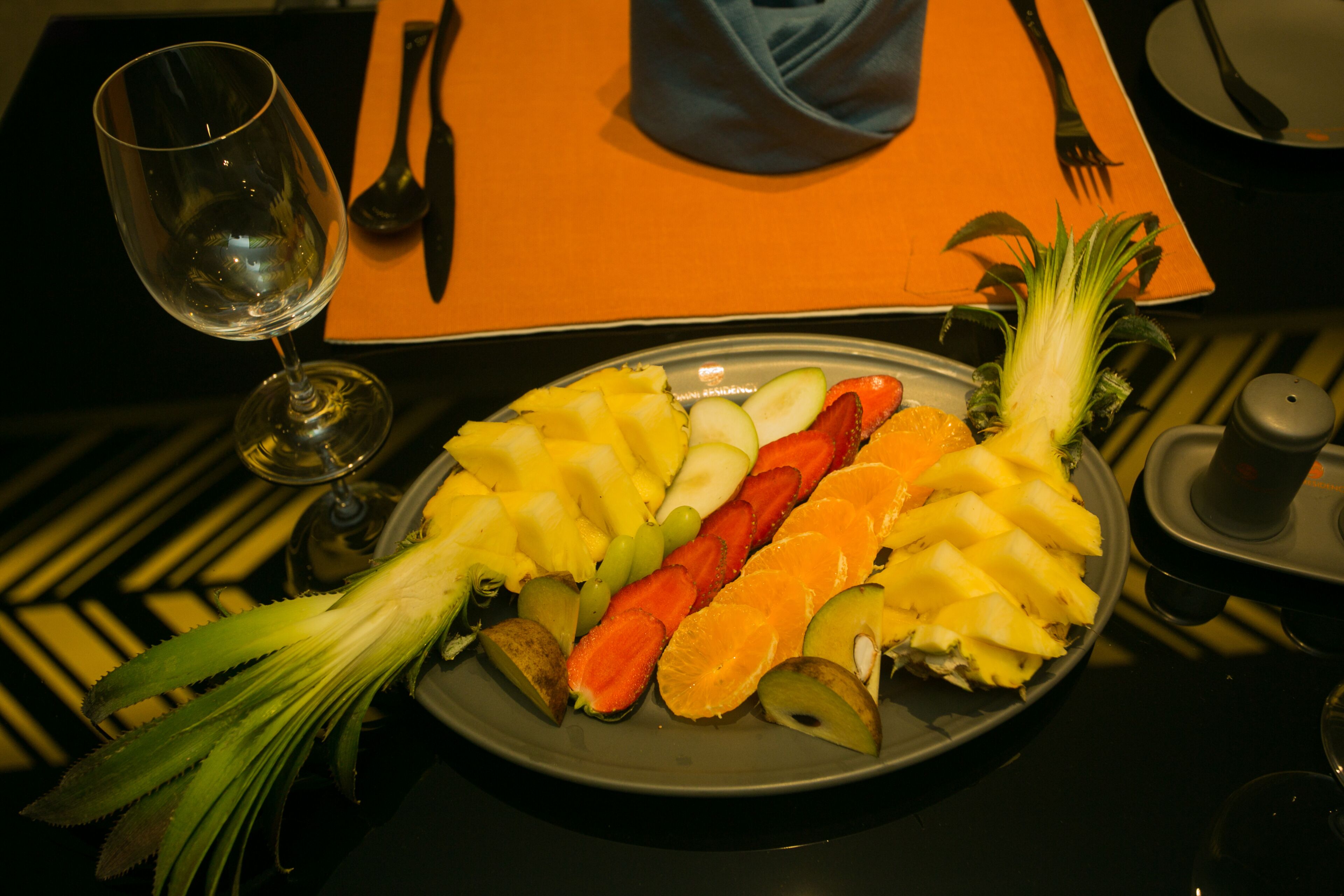 A plate of fruit and a glass of wine on a table with a napkin and cutlery.