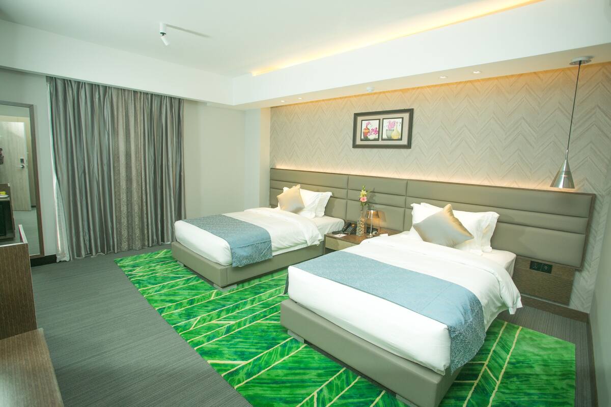 A hotel room with two beds, a desk, and a green patterned rug.
