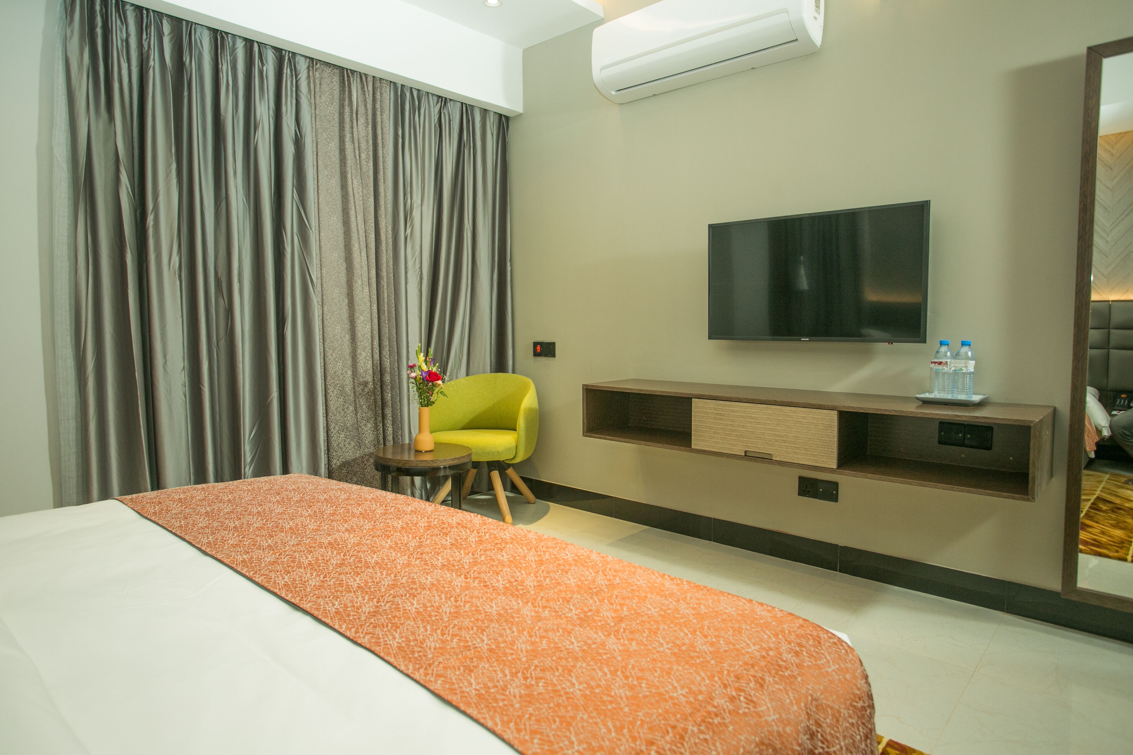 A hotel room with a large bed, a TV mounted on the wall, a small table with a vase of flowers, and a chair.