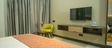 Une chambre d’hôtel avec un grand lit, un téléviseur fixé au mur, une petite table avec un vase de fleurs et une chaise.