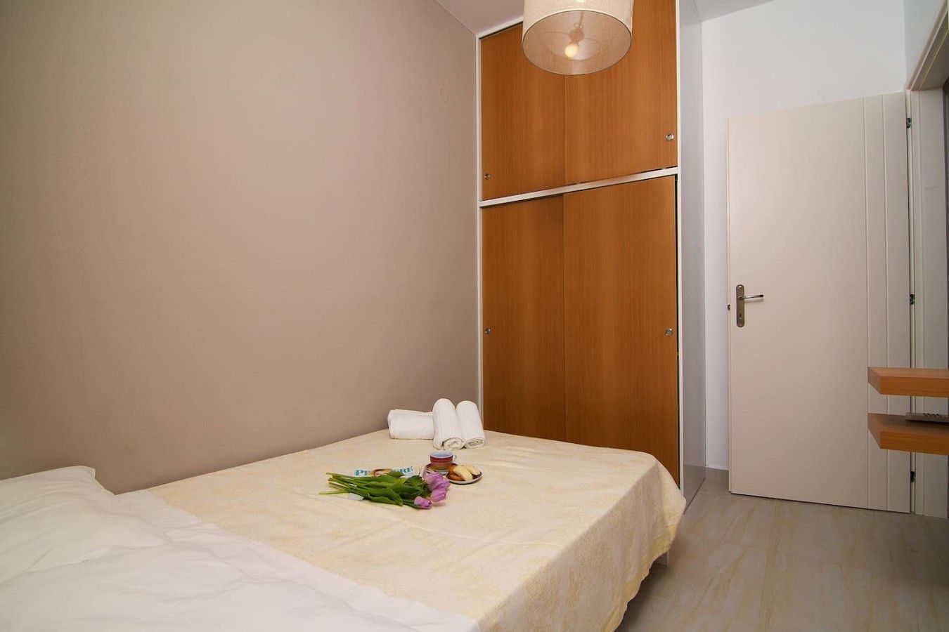 A bedroom with a bed, a wooden wardrobe, and a door.