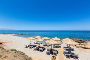 Una spiaggia con lettini e ombrelloni di paglia, cielo sereno e il mare sullo sfondo.