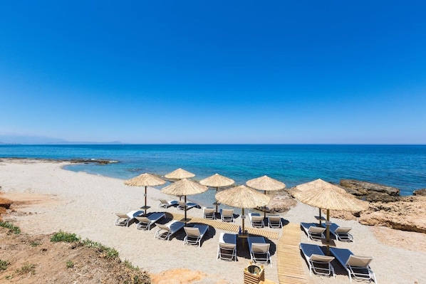 A beach with sun loungers and thatched umbrellas, a clear sky, and the sea in the background.