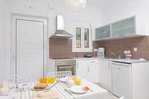 Une cuisine moderne avec des meubles blancs, une cuisinière, un lave-vaisselle et un coin repas comprenant une table, des chaises et des aliments pour le petit-déjeuner.