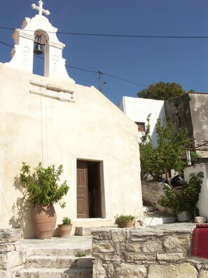 Une église blanche dotée d’un clocher et d’une porte, entourée de plantes en pot et de marches en pierre.