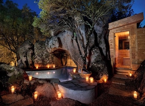 Una cabaña de madera con una piscina de piedra rodeada de velas, ubicada en un área boscosa.