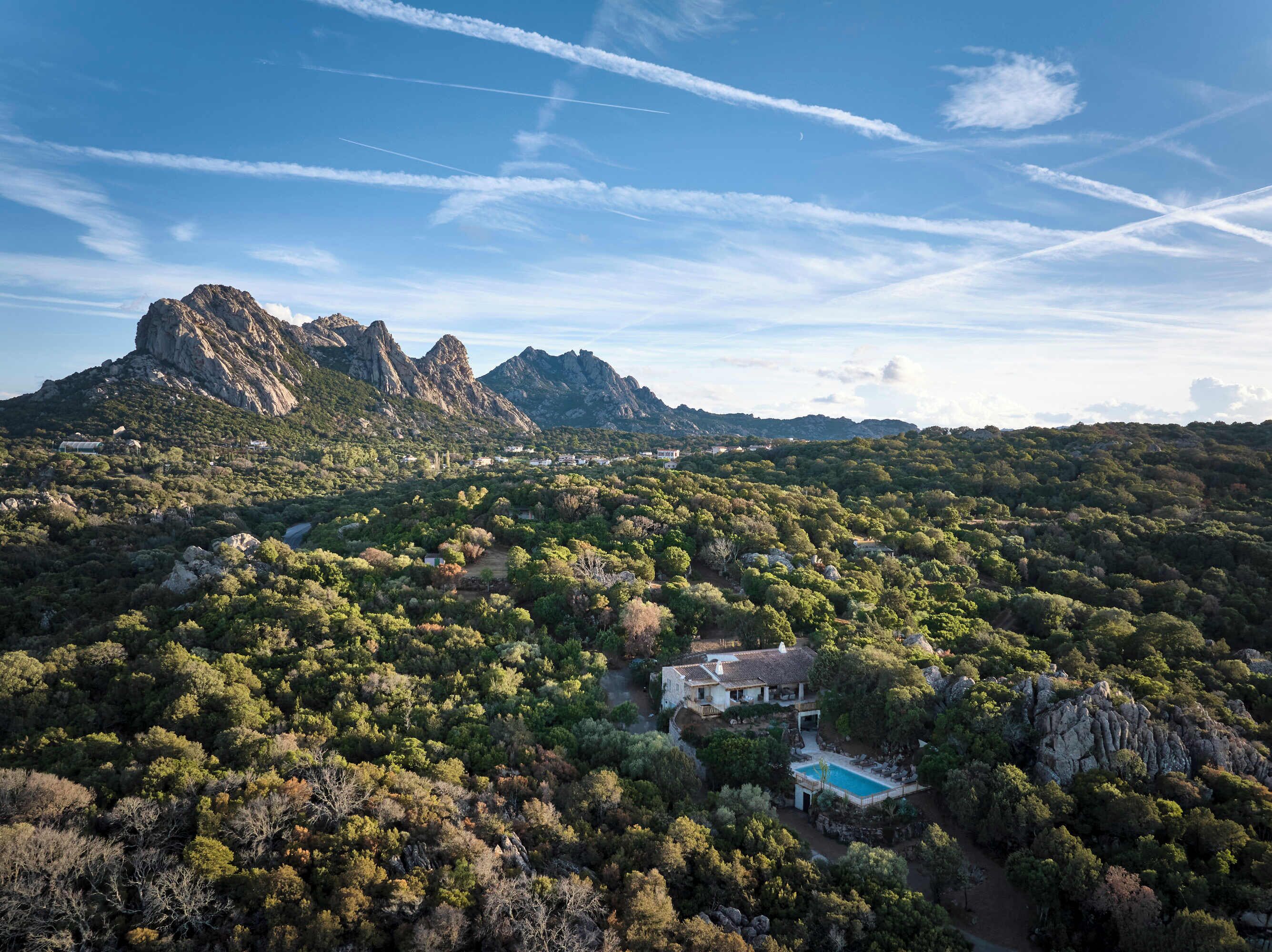 A mountainous landscape with a house featuring a swimming pool surrounded by dense vegetation.
