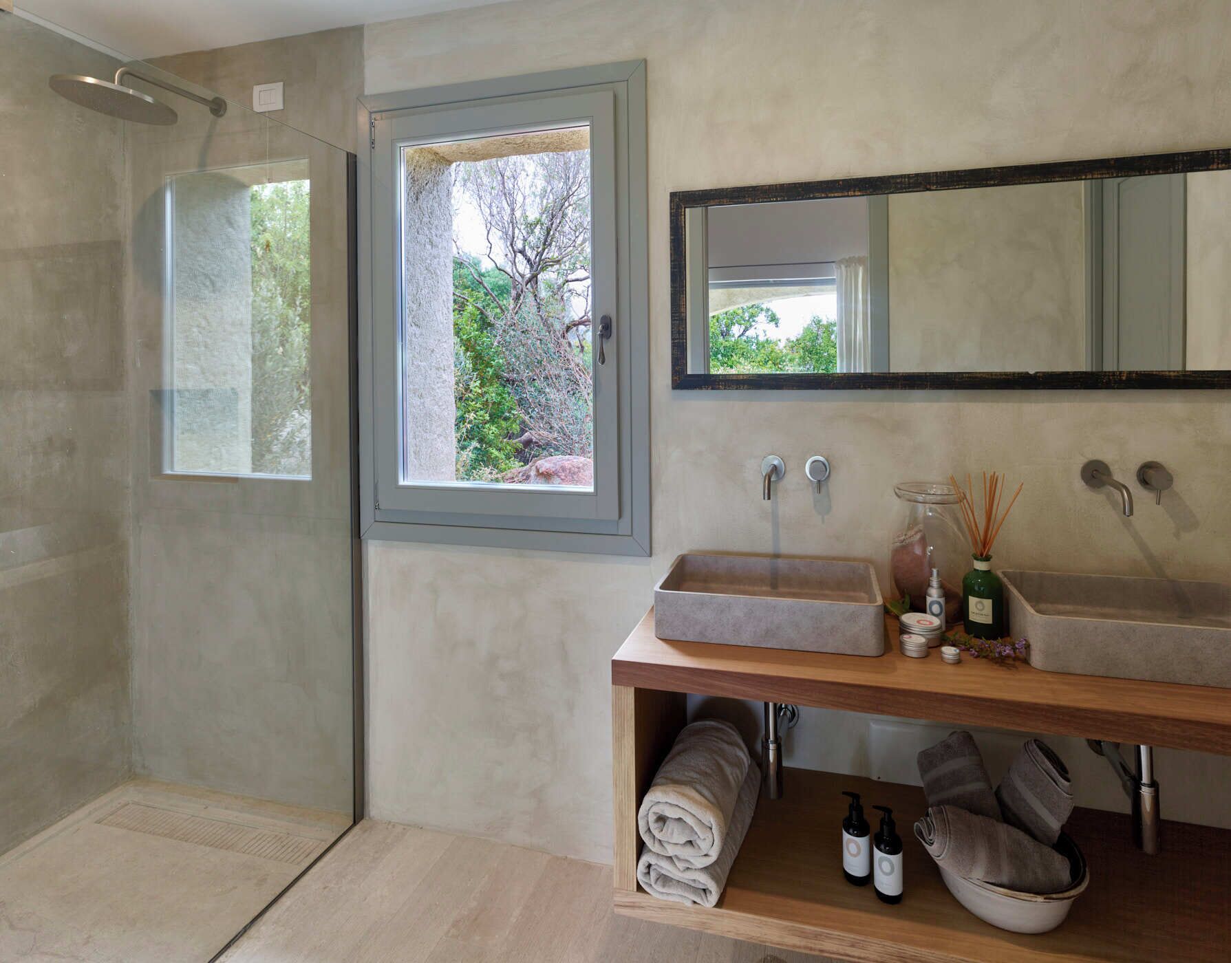 A modern bathroom with a walk-in shower, a large window, two sinks, and a mirror.