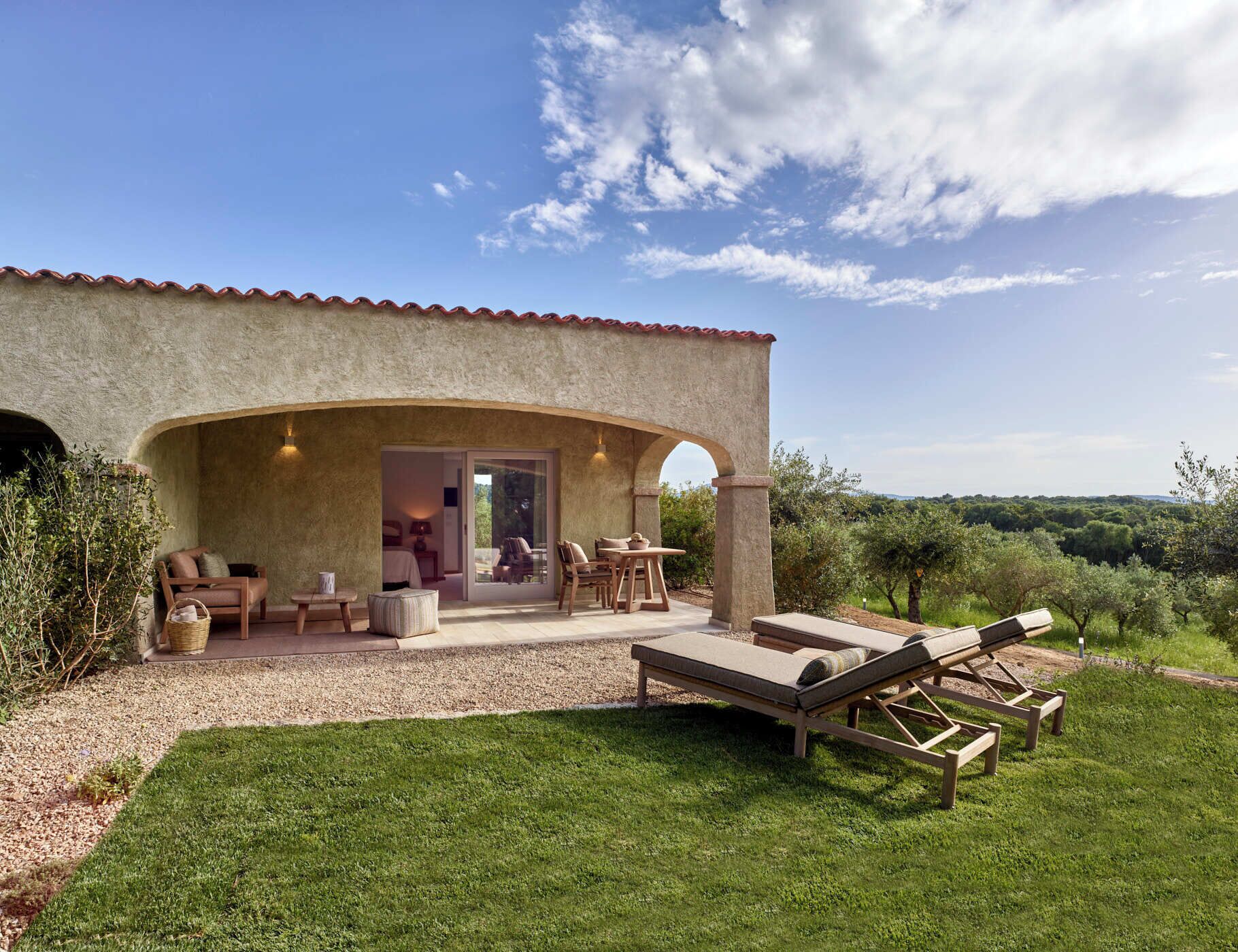 A rustic villa with a patio area featuring outdoor seating, a lounge chair, and a view of the surrounding landscape.