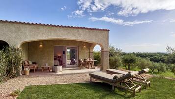 A rustic villa with a patio area featuring outdoor seating, a lounge chair, and a view of the surrounding landscape.
