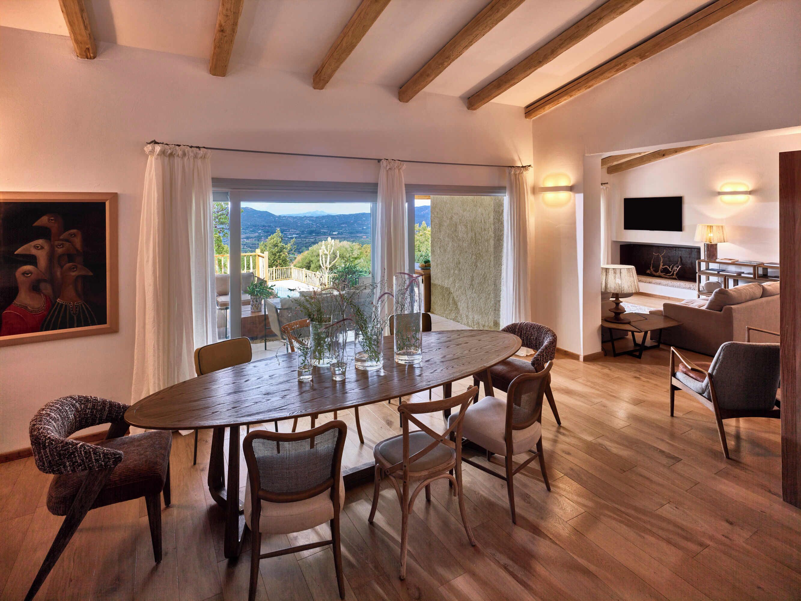 Un comedor con mesa y sillas de madera, ventanas amplias con cortinas, y vistas al exterior.