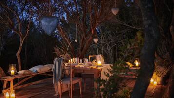 An outdoor dining setup with a wooden table, chairs, candles, and heart-shaped decorations.