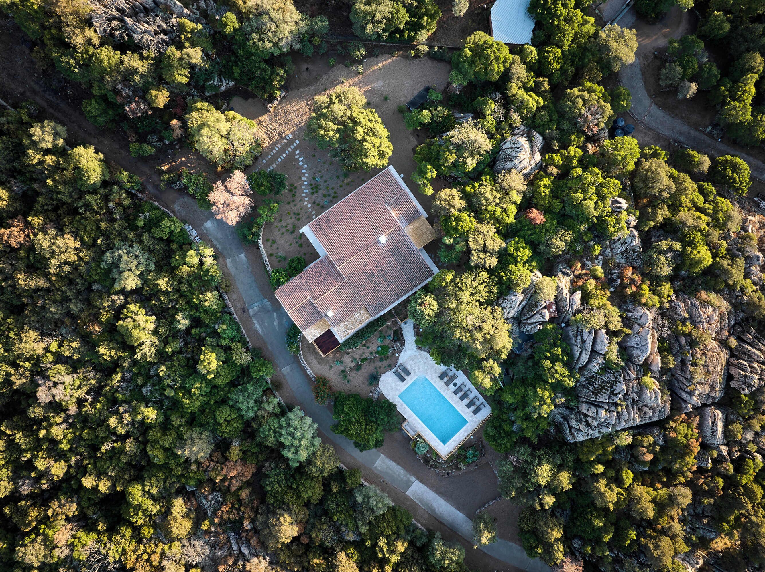 Vue aérienne d’une propriété comprenant un bâtiment principal, une piscine et une végétation luxuriante environnante.