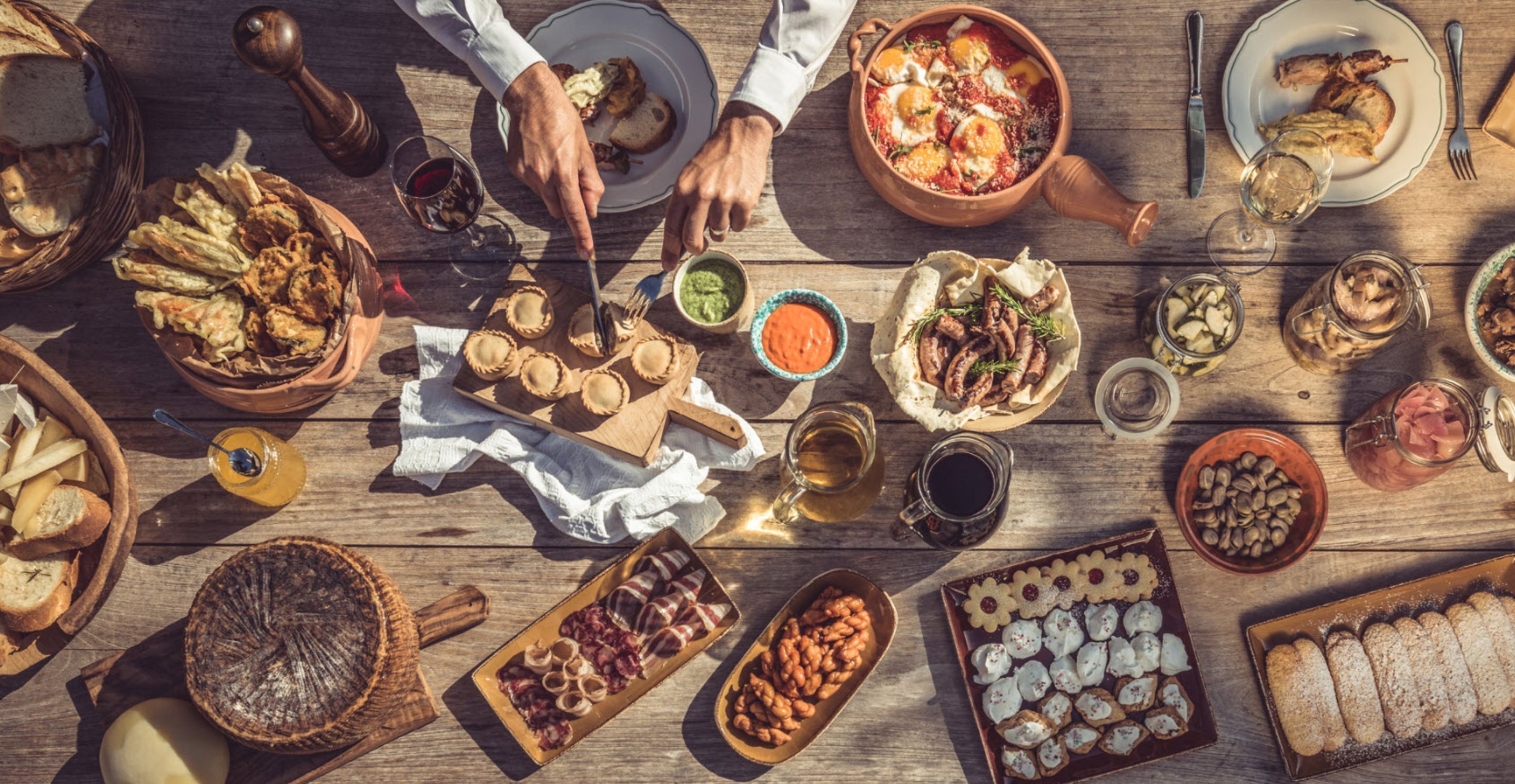 Una mesa de madera con diversos alimentos y bebidas, entre ellos pasteles, carnes y un tazón de sopa.
