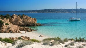Une plage bordée d’une eau turquoise et limpide, de falaises rocheuses et d’un voilier.
