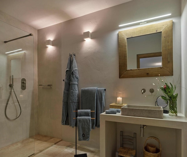 A modern bathroom with a glass shower enclosure, a wooden-framed mirror, a built-in sink, and a small wicker basket. - Cascioni Eco Retreat - Suites with Private Pool (Arzachena)