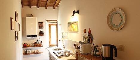 A compact kitchen with a wooden ceiling, a sink, a stove, and a coffee maker.