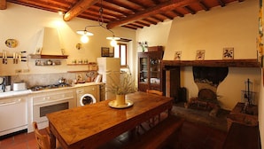 A rustic kitchen with wooden beams, a dining table with a vase, and a fireplace. - 2bedrooms apartment with pool in the Chianti area, organic farm (Florence)