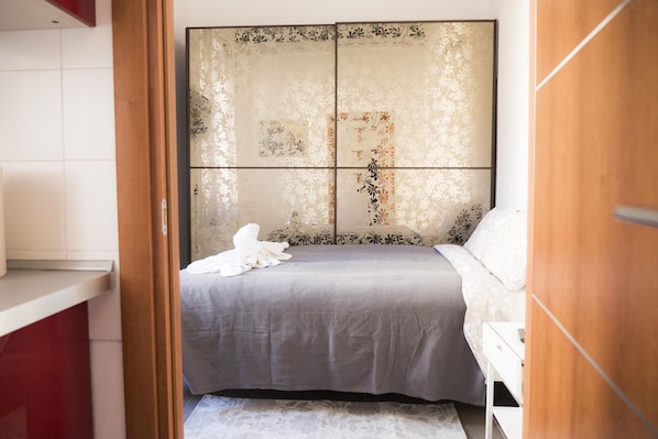 A bedroom with a bed, a wooden wardrobe, and a white bedside table.