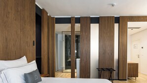 Een moderne hotelkamer met een groot bed, houten lambrisering, een glazen douchecabine en een klein tafeltje.