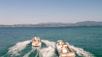Two boats moving through a body of water with a distant shoreline and mountains in the background.