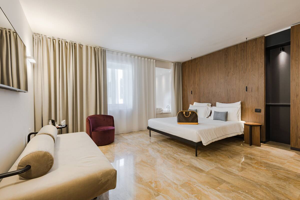 Una habitación de hotel moderna con cama, sofá, sillón y un muro decorativo de madera.