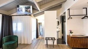 Een moderne hotelkamer met een groene stoel, een houten bankje, een aan het plafond gemonteerde televisie en een houten receptiebalie.