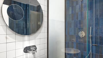 A modern bathroom with a white sink, a round mirror, and a glass-enclosed shower area with blue tiles.