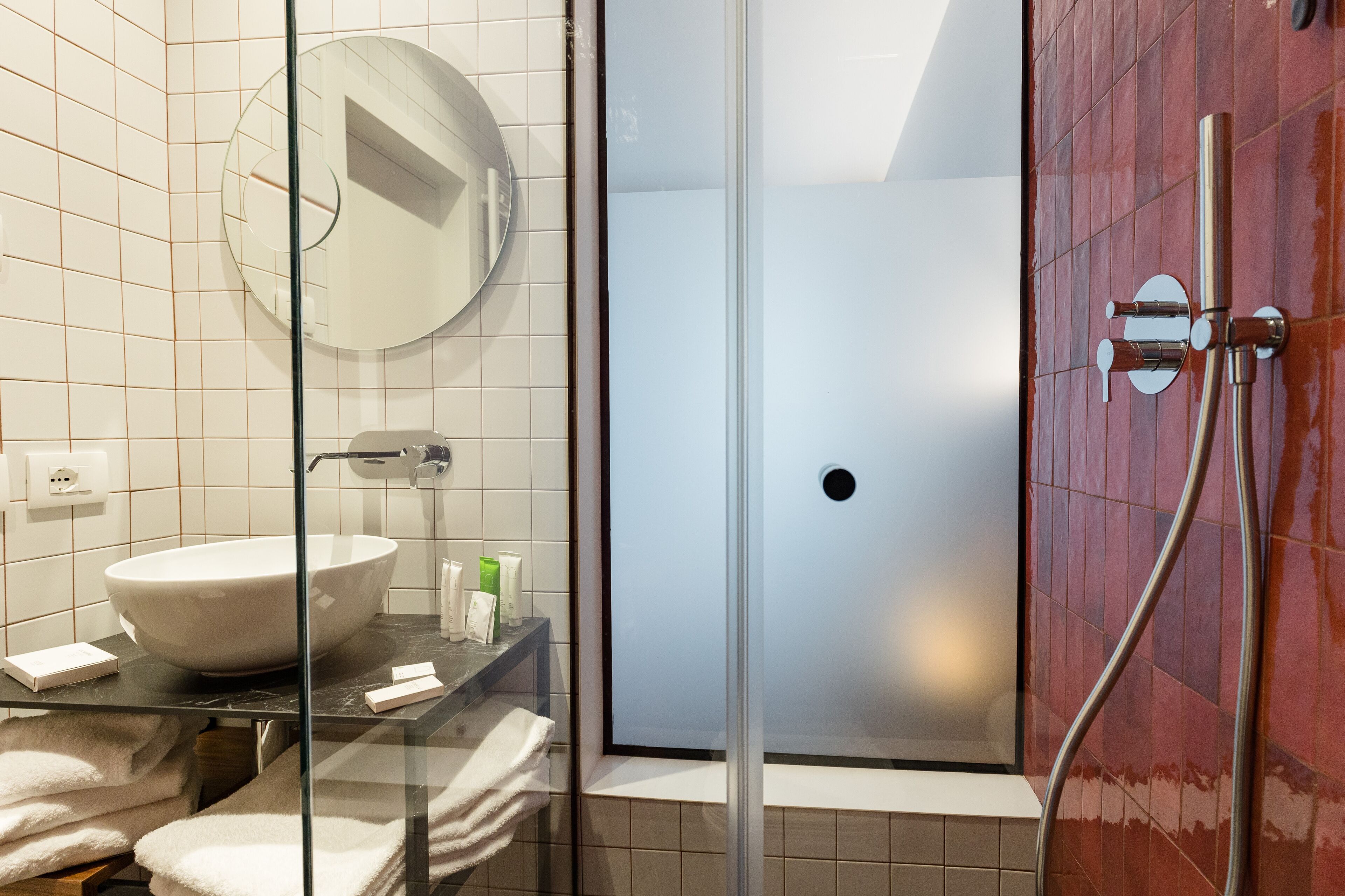 Ein Badezimmer mit einer Duschkabine, einem weißen Waschbecken und einem runden Spiegel.