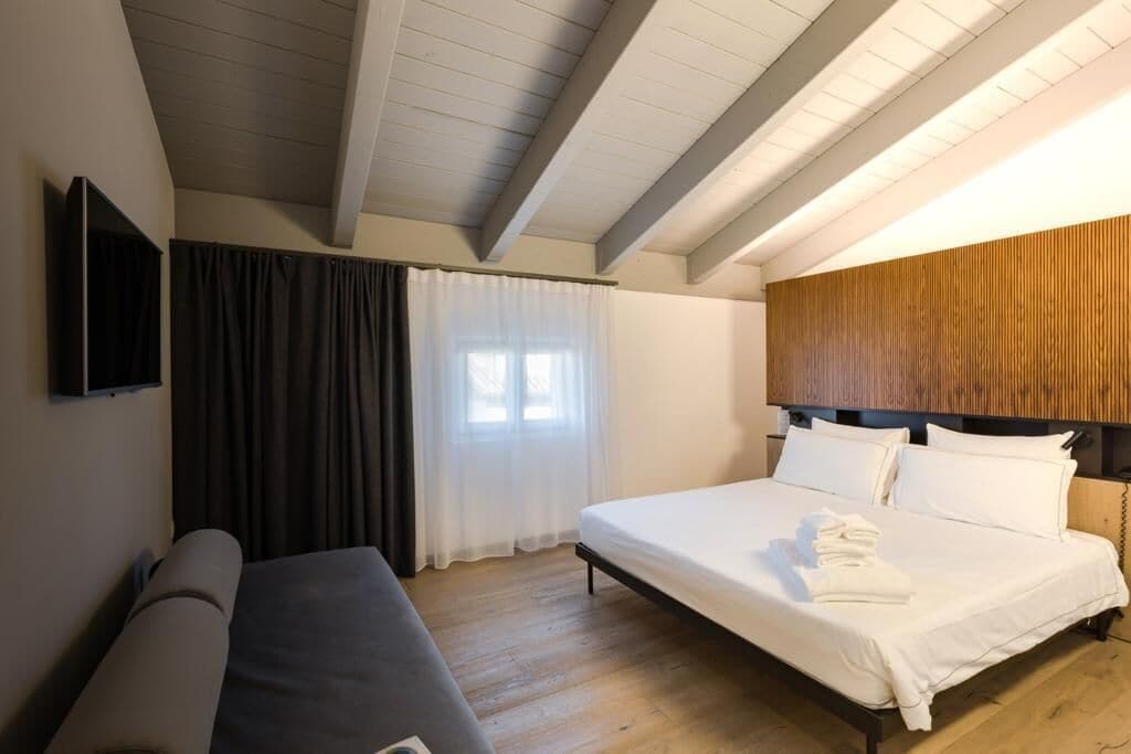 A hotel room with a bed, a sofa, a wooden headboard, and a TV mounted on the wall.