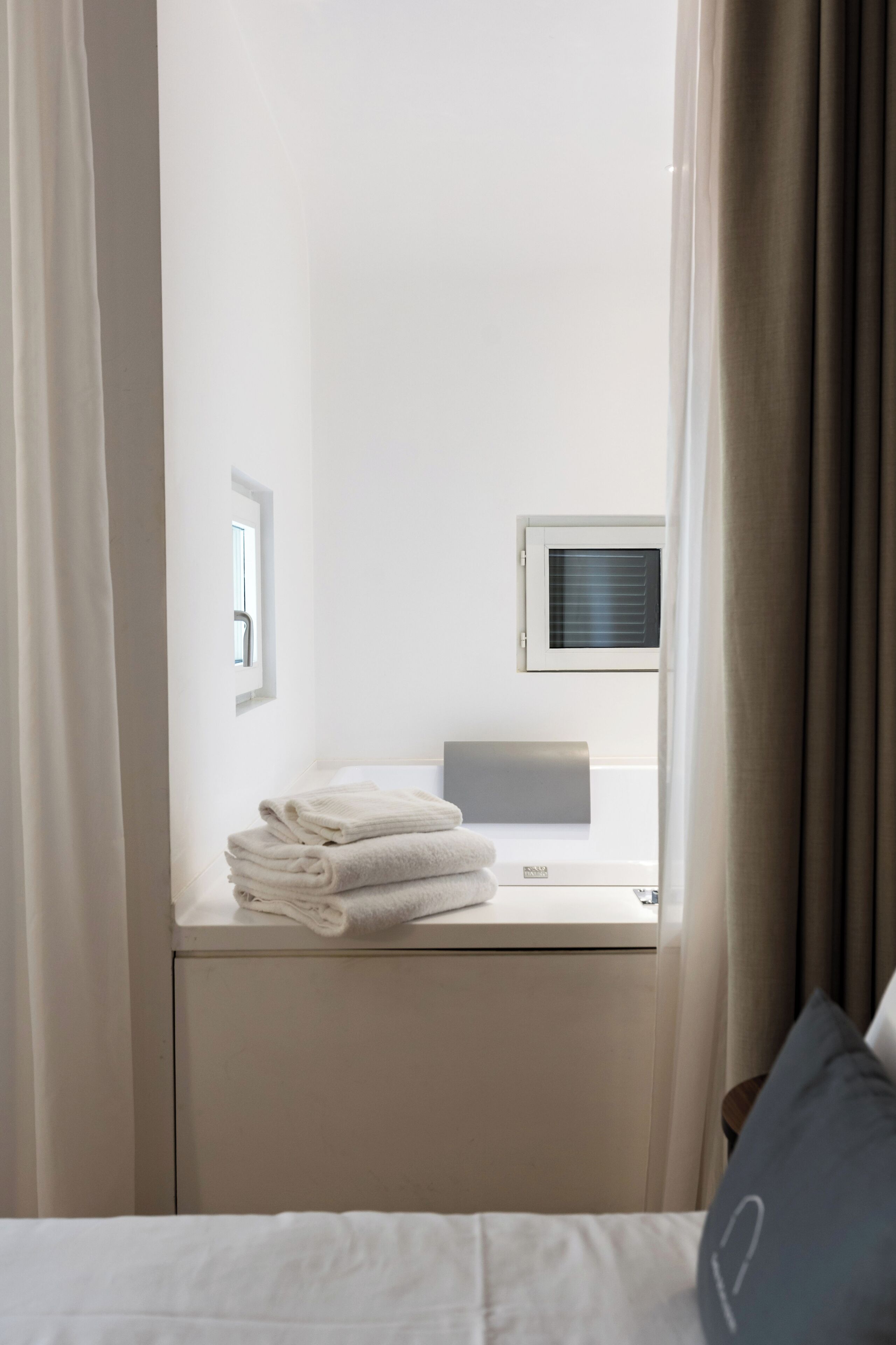 Habitación de hotel con cama, ventana con persianas, una mesita con toallas dobladas y un equipo de aire acondicionado instalado en la pared.