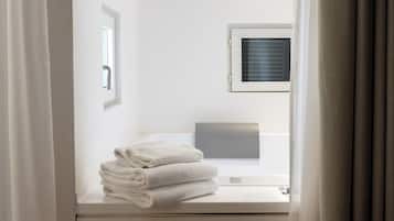Habitación de hotel con cama, ventana con persianas, una mesita con toallas dobladas y un equipo de aire acondicionado instalado en la pared.