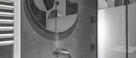 A modern bathroom with a white sink, a round mirror, and a wooden vanity.