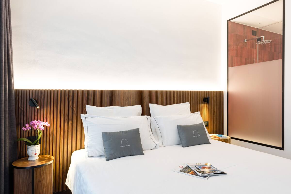 Una habitación de hotel moderna con cabecera de madera, una mesita de noche con un florero y una revista sobre la cama.