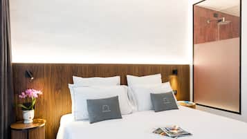 Ein modernes Hotelzimmer mit einem Holzkopfende, einem Nachttisch mit Blumen und einer Zeitschrift auf dem Bett.