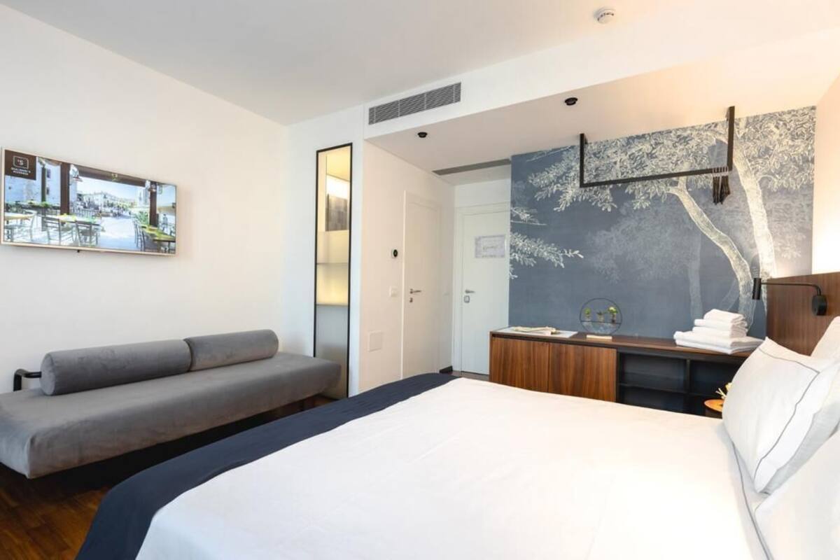 Una habitación de hotel moderna con una cama grande, un sofá, un escritorio con espejo y un televisor montado en la pared.