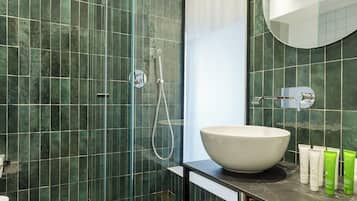 Un baño moderno con ducha envuelta en vidrio, un lavamanos grande tipo cuenco y un mueble de tocador de madera.