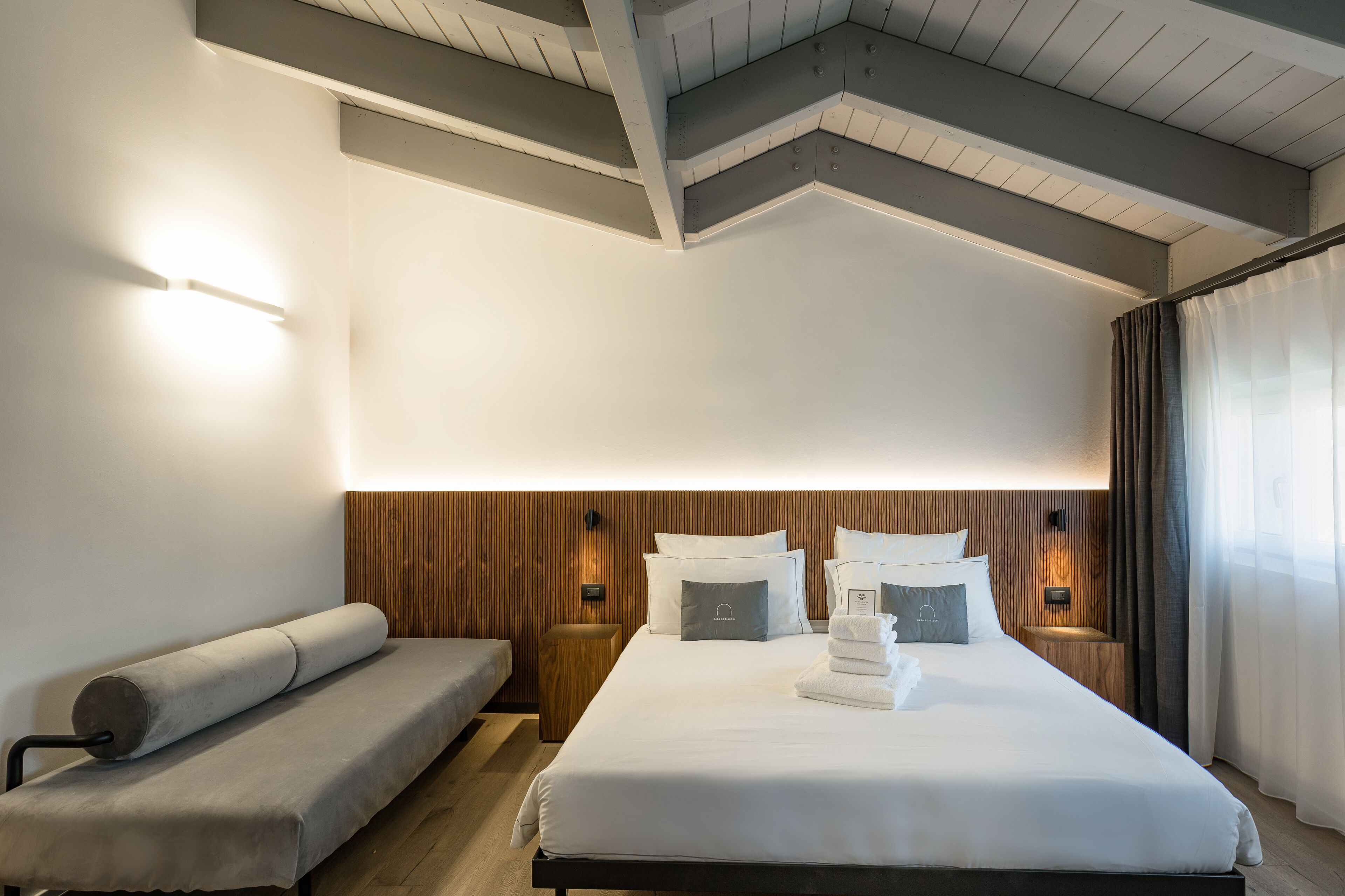 Una habitación de hotel moderna con una cama grande, un banco y un cabecero de madera.