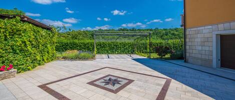 A paved patio with a star-patterned tile design, a pergola, and a view of a lush green landscape under a clear blue sky.