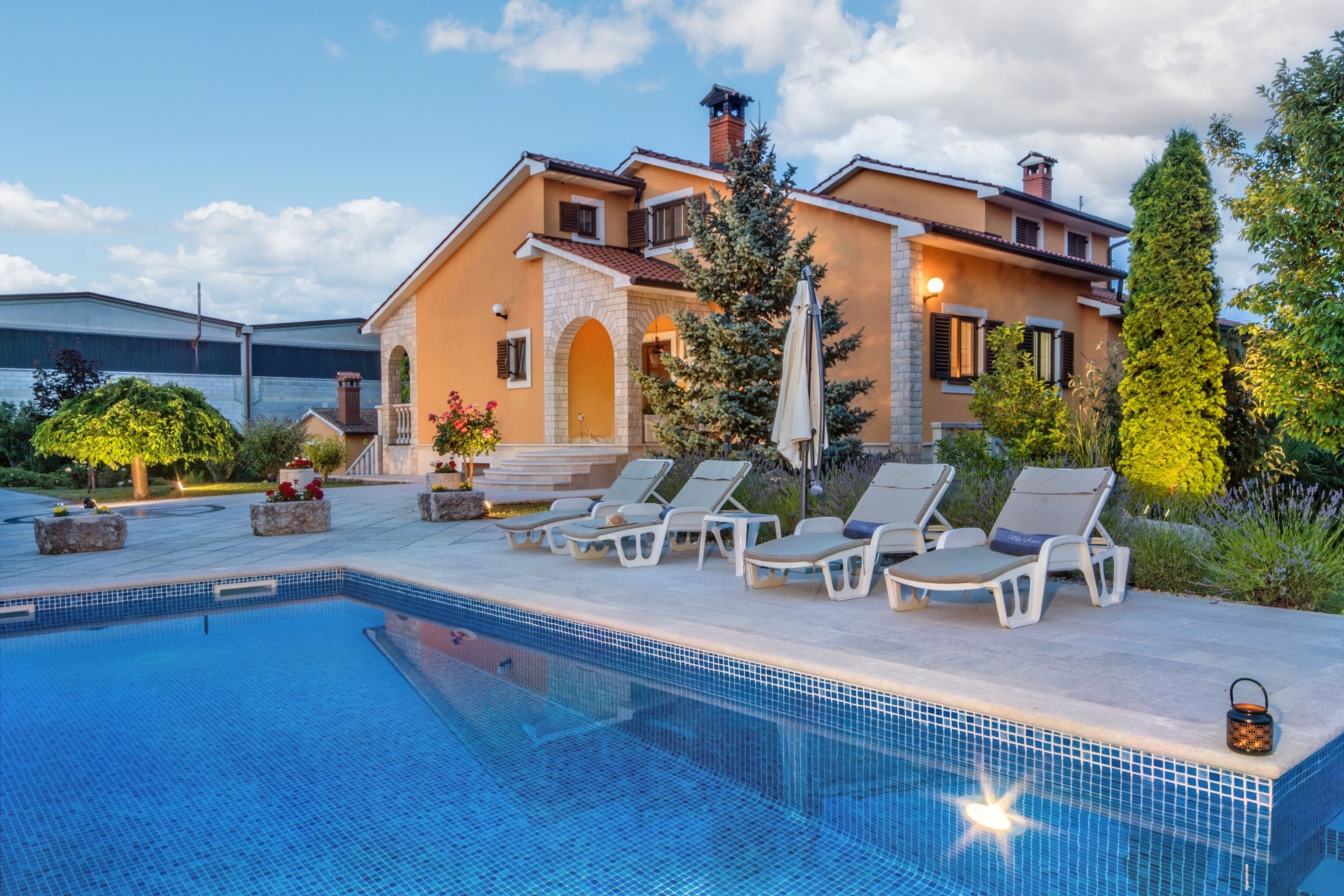 Ein Poolbereich mit Liegestühlen, einem klaren Pool und einem Haus mit Naturstein-Fassade und Schornstein.