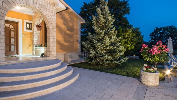 A building with a stone facade, a set of stone steps leading to the entrance, and a well-maintained garden with a large evergreen tree and flower beds. - Wonderful new villa, lush fenced garden, private pool (Pazin)