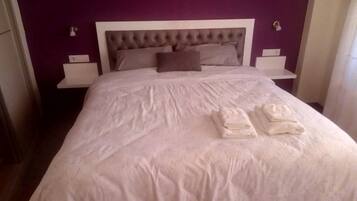 A neatly made bed with a white bedspread and two folded towels, a tufted headboard, and two bedside tables with lamps.