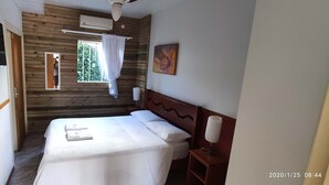 A room with a bed, a TV mounted on the wall, a window with curtains, and a painting on the wall. - Residencial Jade (Florianópolis)