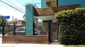 A modern building with a wooden fence, a green hedge, and a sign indicating 'Servidão' and 'Tranquilidade'. - Residencial Jade (Florianópolis)