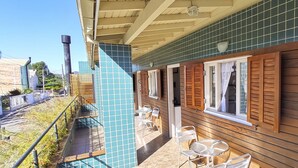 A covered outdoor area with a wooden deck, a small table with chairs, and a view of the street. - Residencial Jade (Florianópolis)