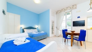 Une chambre d’hôtel avec un lit, une table à manger avec des chaises, un téléviseur et une fenêtre avec des rideaux.