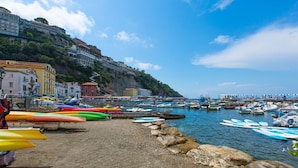 Une ville côtière où l’on peut admirer des kayaks aux couleurs vives alignés sur la plage, des bateaux amarrés dans l’eau et des bâtiments construits sur une colline.